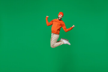 Wall Mural - Full body young exultant happy overjoyed excited fun cool man 20s in orange sweatshirt hat jump high clench fist celebrate isolated on plain green background studio portrait. People lifestyle concept.