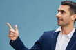 © SHOTPRIME STUDIO - cheerful man on suit look aside pointing finger up successful career job blue isolated background Copy space