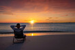 © moofushi - A man on vacation relaxes in a sun chair on a tropical beach during colorful sunset time