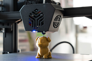 Detail of a 3D printer printing a model with a gold biodegradable PLA filament, ecofil, blue light