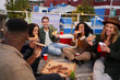 © StratfordProductions - Group of multi-cultural young adult friends eating pizza while sitting on a rooftop in the city.