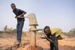 A diligent black youngster pumping fresh drinking water for his thirsty little brother at a public manual faucet somewhere in West Africa
