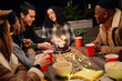 © StratfordProductions - Group of diverse young adults sitting at boho themed rooftop party celebrating birthday girl with cake.