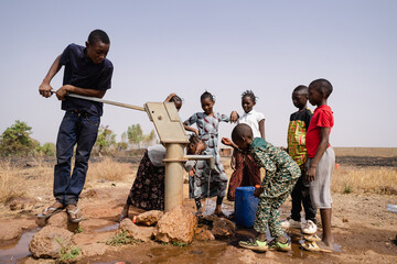 group of black african school age children gathering around a sub saharian village faucet collecting