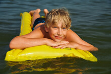 Teen Boy Swimming On Air Mattress In The Sea And Enjoying Summer Vacation