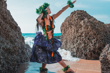 Gorgeous woman dressed in traditional Hawaiian dance attire enjoying views of a spectacular paradise beach. Woman on the rocks poses. Young lady dancing hula dance.