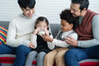 © Pruksachat - Happy young Asian gay couple with diverse adopted children, African and Caucasian, drinking milk and sitting on sofa at home. Older boy with milk mustache cheer up little girl drink milk. Lgbt family