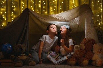 children boy and girl playing and frighten each other with flashlight in tent at night