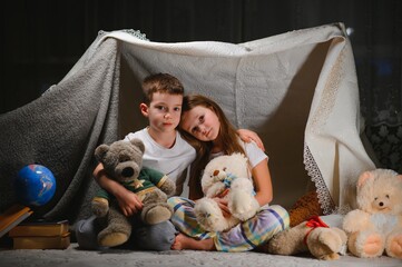 reading and family games in children's tent. boy and girl with book and flashlight before going to bed