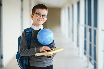 Wall Mural - Happy cute clever boy in glasses with school bag and book in his hand. First time to school. Back to school.