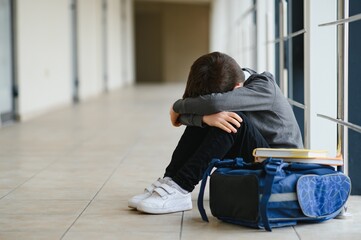 Upset boy sitting at school and crying after bullying by pupils classmates. The child covered his face with his hands and cries.