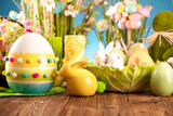 Fototapeta Storczyk - Easter time. Easter decorations on the rustic wooden table. Easter bunny, easter eggs in basket and cabbage leaf. Bouquets of spring flowers. 