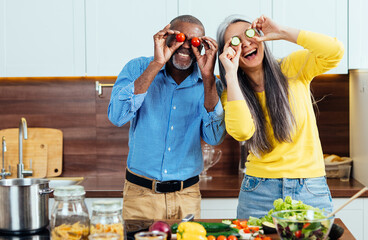 cinematic image of a multiethnic senior couple preparing food in the kitchen. Indoors Lifestyle moments at home. Concept about seniority and relationships