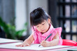 © Kanthita - Portrait Asian kid sitting on large sheet of drawing paper on table. Students concentrate on art work. 4 year old girl wears pink shirt with white polka dots. Kindergarten child in homeschool class.