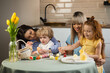 © Andrii  - Two mothers with their children coloring Easter eggs while sitting in the kitchen