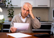 Old Gray Haired Man Sitting At Table And Stunned Notice On White Sheet