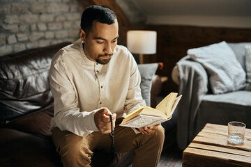 Wall Mural - Middle Eastern man holds prayer beads while reading Koran at home.