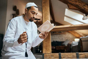 Wall Mural - Muslim man reads from Koran and holds misbaha beads while praying at home.