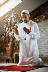 Wall Mural - Middle Eastern man kneeling on prayer carpet while praying at home.