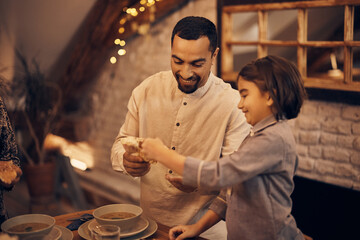 Happy Muslim father and daughter share pita bread while eating dinner on Ramadan at home.