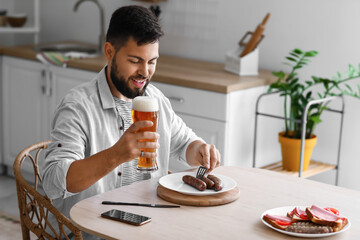 Poster - Handsome bearded man with glass of beer sitting at dining table in kitchen