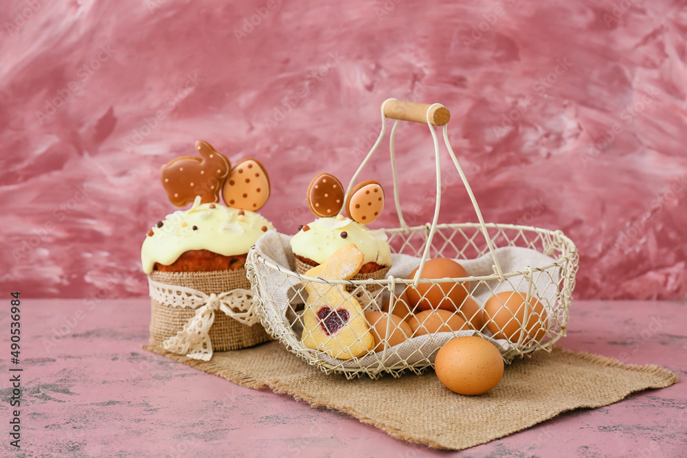 Gift basket with eggs, cookie and Easter cakes on pink background