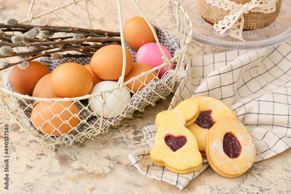 Gift basket with painted Easter eggs, pussy willow branches and cookies on beige background
