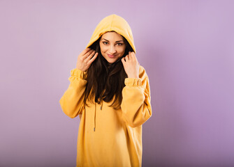 Canvas Print - Relaxing thinking smiling sporty woman posing in fashion yellow hoodie on purple bright background with empty copy space. Happy