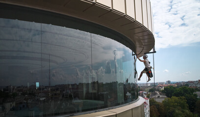 Wall Mural - Industrial mountaineering worker professional window washer hanging on climbing rope and cleaning glass window of skyscraper. Male cleaner washing window of high-rise building.