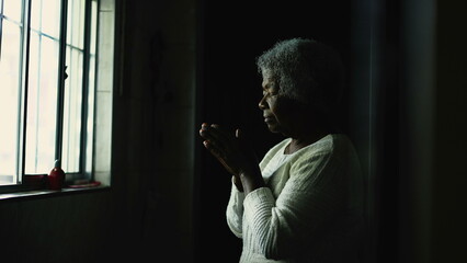 A Spiritual young African woman praying to God at home standing by window