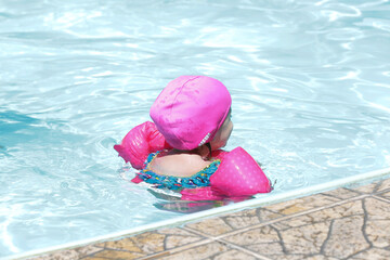 Child in the pool swimming with pink float with blue water.