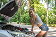 beautiful girl wear short shorts and t-shirts  looking into engine compartment of broken down car