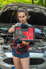 Wall Mural - beautiful pretty brunette dressed in summer repairs a car on the road with an open hood.