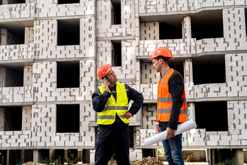 workers are strong in overalls and helmets with a plan in hand standing near the new building