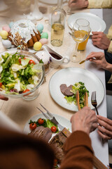 cropped view of family near vegetable salad and easter cake on served table.