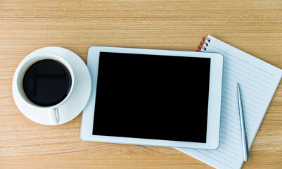 Digital tablet with coffee, paper and pen on wooden table