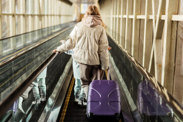 Wall Mural - Mom and daughter go up the escalator to the building of the station or airport