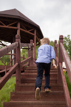 The Boy Climbs The Wooden Stairs In The Park. Cloudy, The Child Runs Up The Stairs To The Veranda. Spring In The Park.