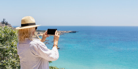 Wall Mural - A tourist woman in a white dress and with hat enjoys the beautiful, turquoise Sea of Greece during her summer holiday. Banner with copy space.