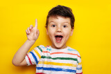 idea. child, boy emotionally points up. A gesture of an idea. Portrait of a child in a bright striped T-shirt on a yellow background