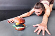 Willpower. Fitness woman trains willpower. Athletic girl tempts herself with a delicious burger at a fitness workout. The concept of weight loss and willpower training.