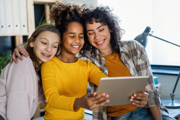 Wall Mural - Diverse ethnicity student girls, sisters using a digital gadgets, having fun or studying together.