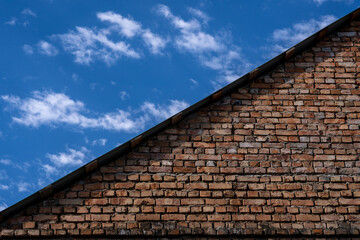 a large old brick part of the roof of a building that forms a triangle dividing the picture into two parts where there is a beautiful blue sky with white clouds