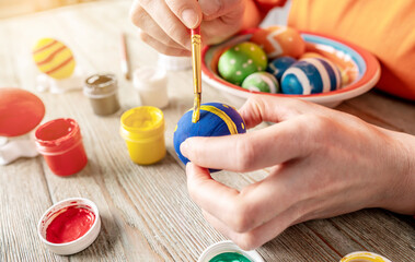 Wall Mural - Hand with a brush is drawing a colored pattern on an Easter egg. Creative preparation for bright Easter holiday