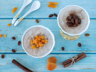 Homemade sweet white rice pudding in two ceramic bowls with cinnamon, raisins, and dried apricots on a light blue wooden table and cinnamon sticks. Creamy vegan dessert from Turkish cuisine. Top view.