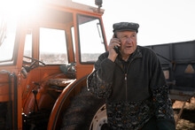 Senior Man Talking On Smartphone Near Tractor In Field