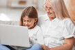 © Pixel-Shot - Little girl with her grandma using laptop on sofa at home