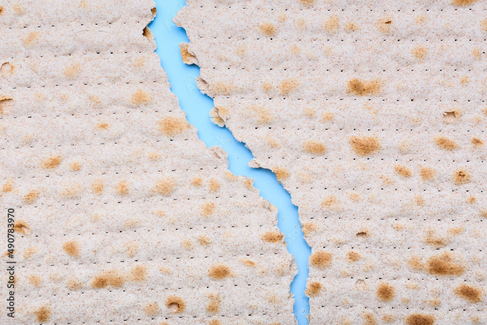 Torn Jewish flatbread matza for Passover on blue background, closeup