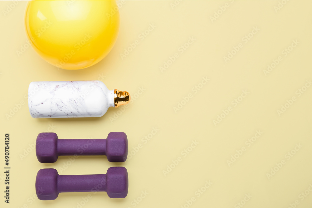 Stylish dumbbells, bottle and ball on yellow background