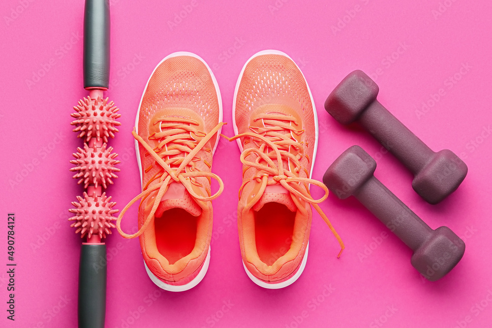 Stylish dumbbells, shoes and massage roller on pink background